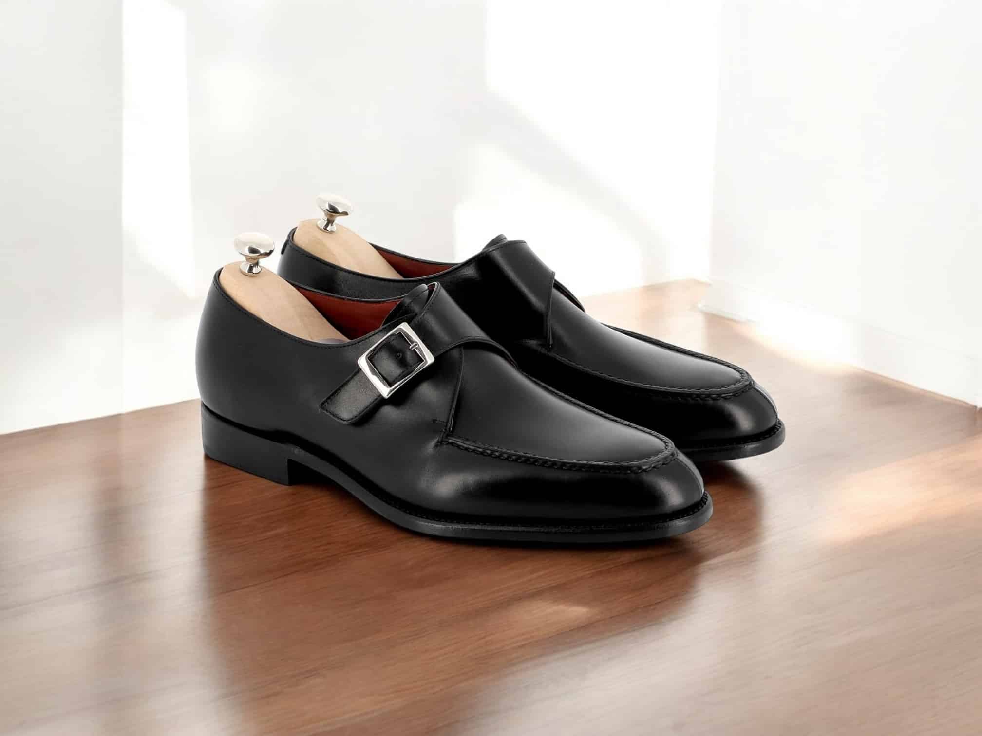 Chaussures noires en cuir avec boucle, sur plancher.